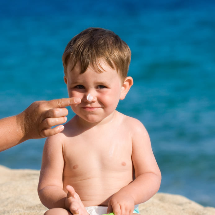 Father spreading suntan lotion on his son's face.